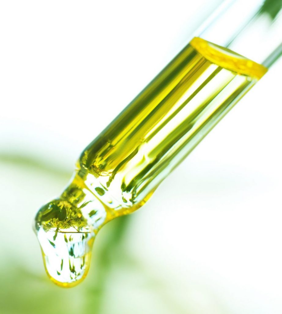 Glass dropper pipette with golden yellow essential oil drop falling, set against a soft green blurred background.