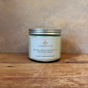Gingerlilies 'Revitalising' Essential Oil Candle with a silver screw-top lid, featuring a white label with bergamot, cypress, and black pepper ingredients, displayed on rustic wood flooring.