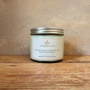 Gingerlilies 'Tranquillity' Essential Oil Candle with a silver screw-top lid, featuring a white label highlighting peppermint, lavender, and litsea scents, displayed on rustic wood flooring.