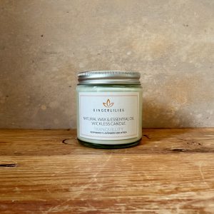 Gingerlilies 'Tranquillity' Essential Oil Candle with a silver screw-top lid, featuring a white label highlighting peppermint, lavender, and litsea scents, displayed on rustic wood flooring.
